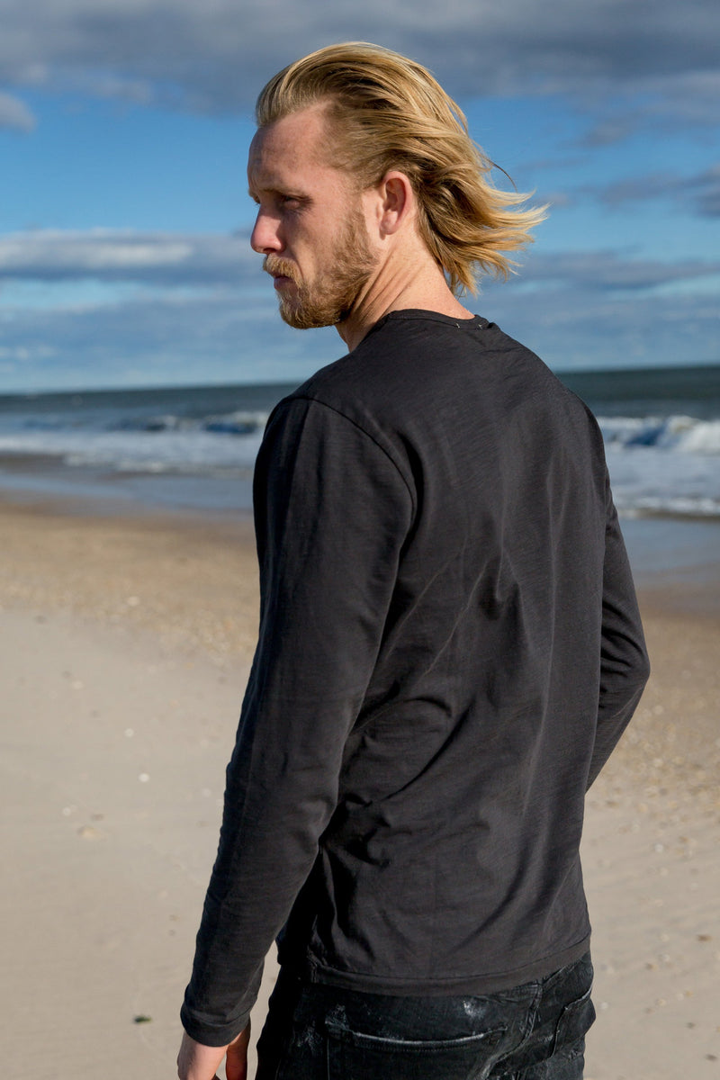 Man modeling the back of Standard Slub Long Sleeve Tee in black, on the beach